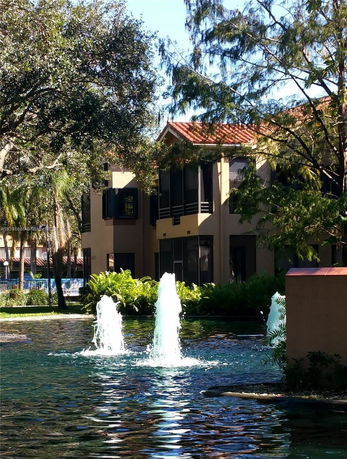 View of a building with a pond and water fountains, surrounded by trees.