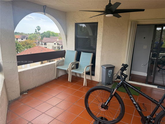 Outdoor balcony area with chairs and a bicycle, overlooking a residential neighborhood with tiled roofs.