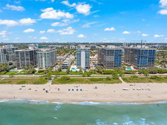 Aerial view of beachfront buildings with a sandy beach and ocean in the foreground.