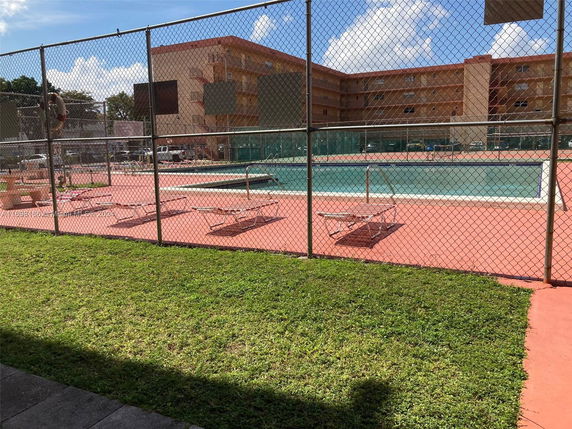 Outdoor swimming pool area with a fence and sun loungers near a multi-story building.