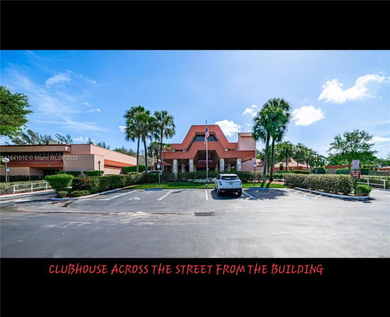 Front view of a clubhouse with parking area and palm trees.