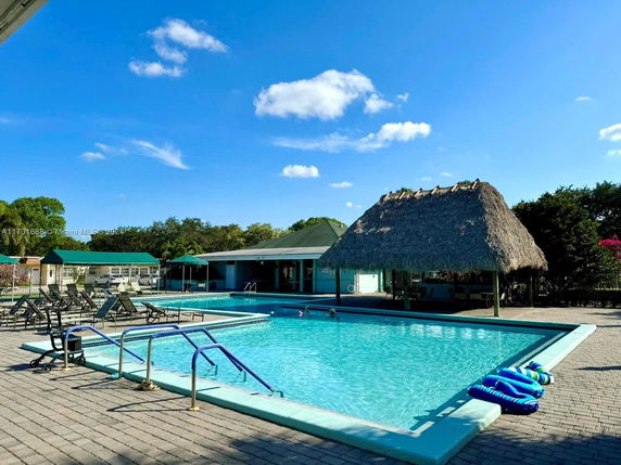 Outdoor swimming pool with lounge chairs and a thatched-roof structure nearby.