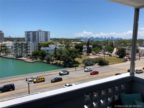 View from a balcony overlooking a road, nearby buildings, and a waterfront area with city skyline in the distance.