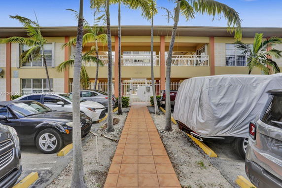 Front view of a two-story building with a walkway and parked cars.