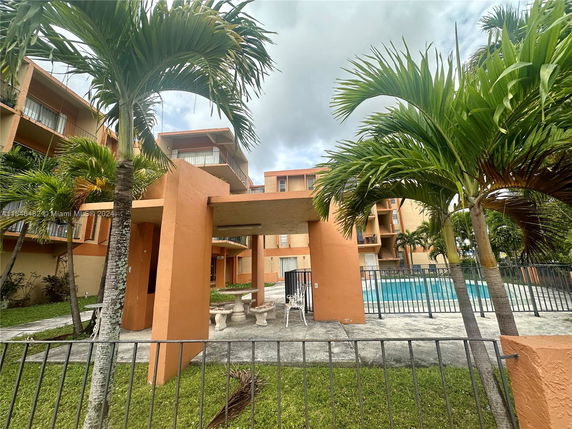 Outdoor view of a multi-story apartment building with a swimming pool and palm trees in the foreground.