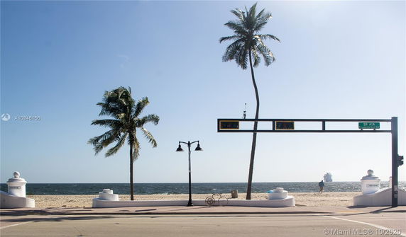 View of a beach with palm trees, a street lamp, and a traffic signal near Fort Lauderdale Beach Boulevard.