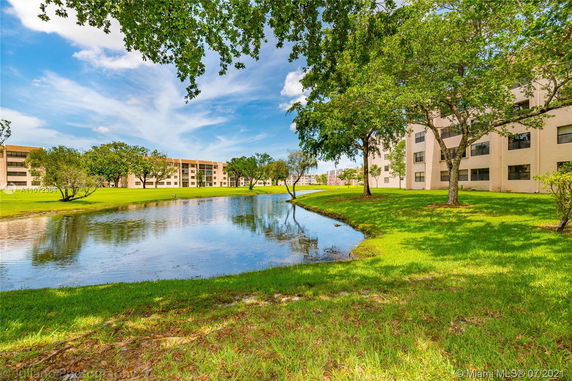 View of apartment buildings next to a pond with trees and grass.