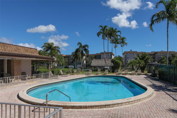Outdoor swimming pool area with surrounding lounge chairs and palm trees.