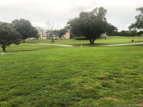 View of grassy area with trees and a multi-story building in the background.