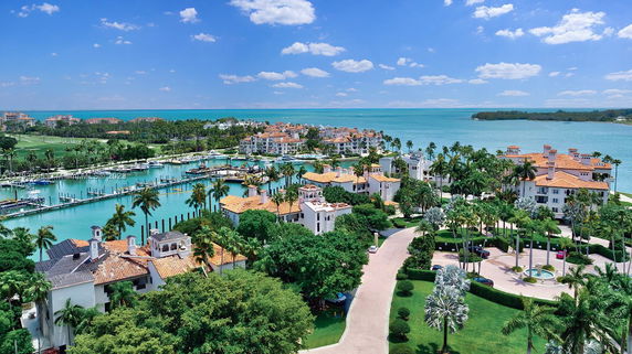 Panoramic view of a coastal community with multiple buildings, marina, and surrounding greenery.