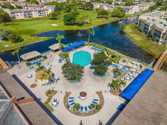 Aerial view of a swimming pool area with lounge chairs and umbrellas, surrounded by water bodies and residential buildings.