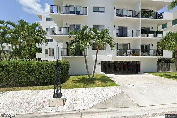 Front view of a multi-story apartment building with balconies and palm trees.