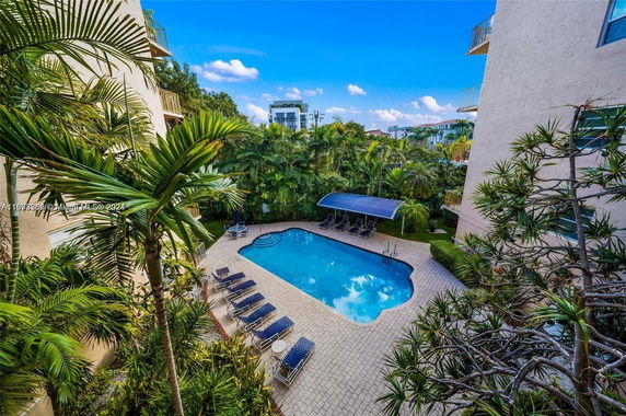Outdoor swimming pool area surrounded by buildings and palm trees.