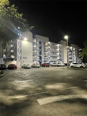 Night view of a multi-story residential building with a parking area in front.