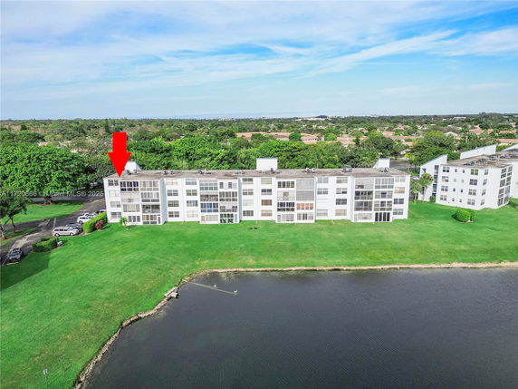 Aerial view of a large multi-story residential building near a body of water, with grassy surroundings.
