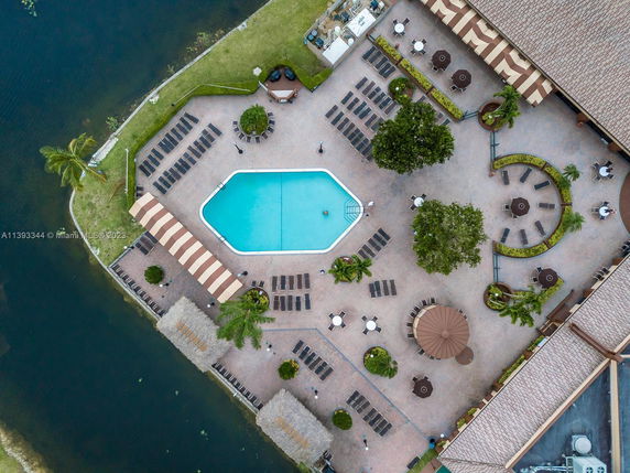 Aerial view of an outdoor swimming pool area with sun loungers and umbrellas, adjacent to a body of water.