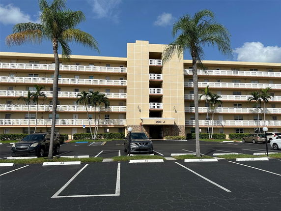 Front view of a multi-story residential building with multiple balconies and a parking area.