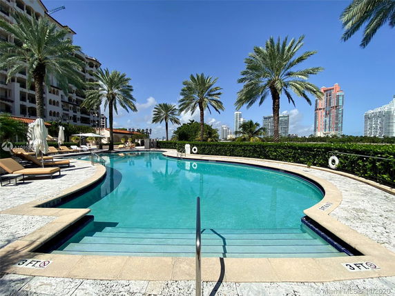 Outdoor swimming pool area with palm trees and surrounding high-rise buildings.