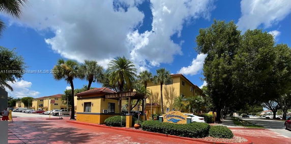 Front view of a yellow multi-story building with palm trees.