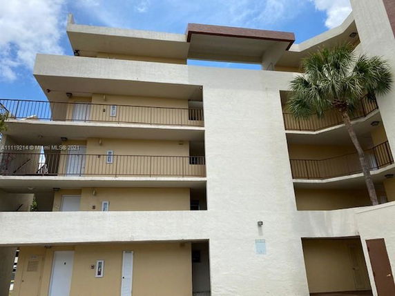 Front view of a multi-story building with balconies and a palm tree.
