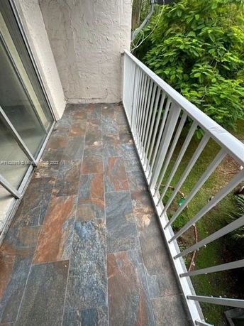 View from a balcony with tiled floor and metal railing overlooking greenery.