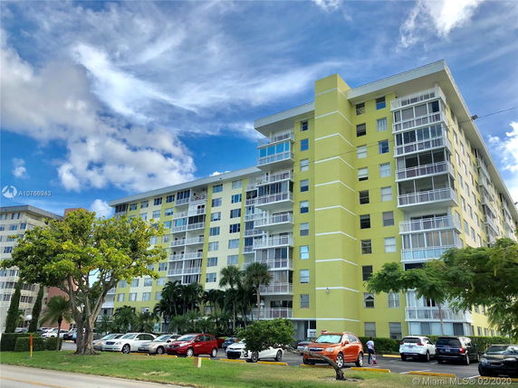 Front view of a multi-story apartment building with balconies and yellow exterior.