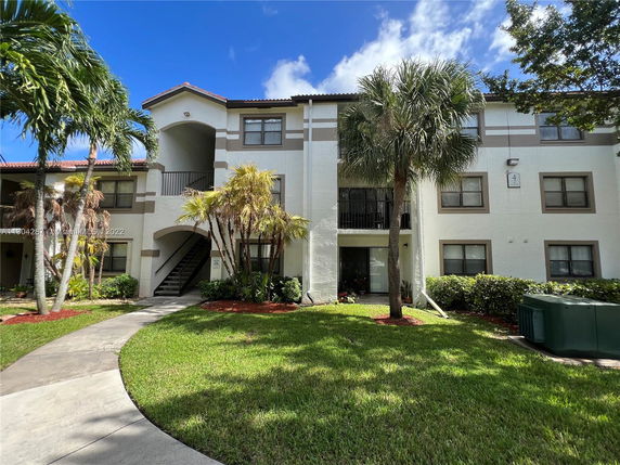 Front view of a two-story apartment building with a central staircase and surrounding palm trees.