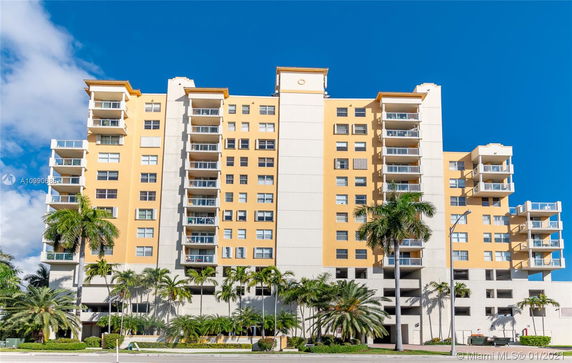 Front view of a mid-rise residential building with multiple balconies and palm trees.