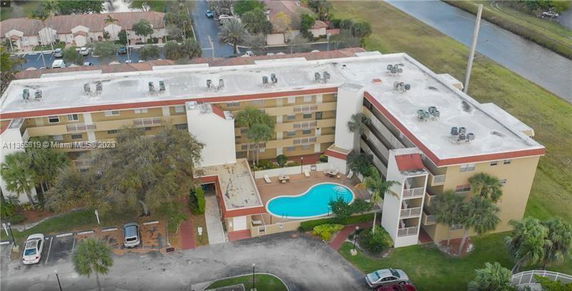 Aerial view of a multi-story apartment building with a swimming pool at the center and multiple utility units on the rooftop.