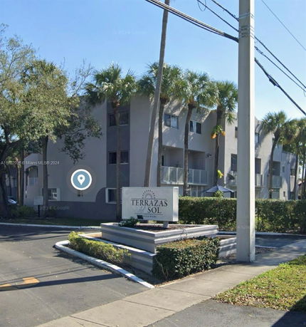 Front view of a multi-story building with balconies and palm trees.