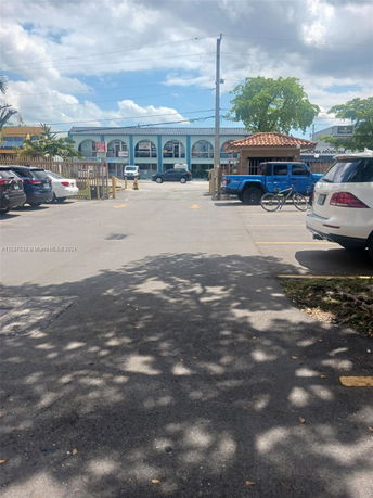 Outdoor parking area with cars and a small building in the background.