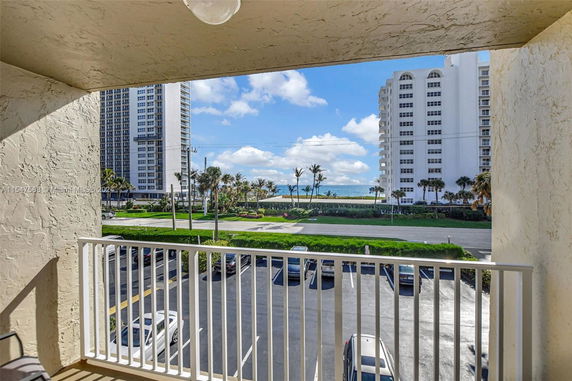View from a balcony overlooking parking area, with tall buildings and the ocean in the background.