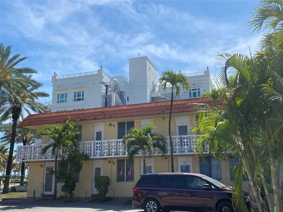 Front view of a two-story building with a decorative balcony and palm trees.