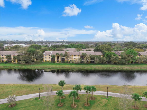 Aerial view of residential buildings surrounded by trees with a lake in the foreground.