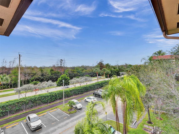 View from a building overlooking a parking area and a road lined with trees.