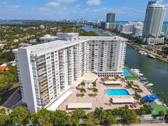 Elevated view of a tall residential building with balconies, adjacent swimming pool, and surrounding area.