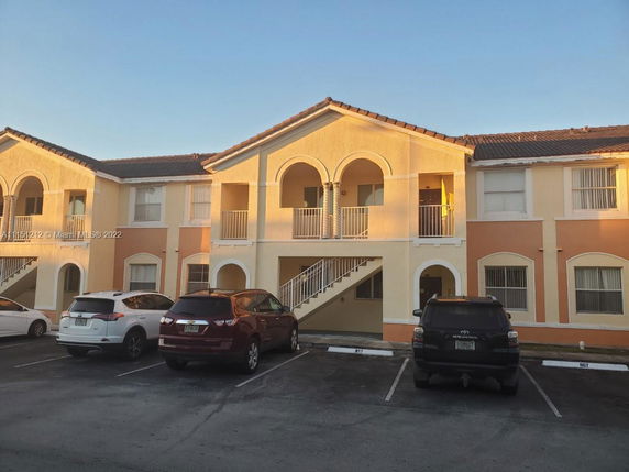 Front view of a two-story residential building with arched balconies and a parking area in front.