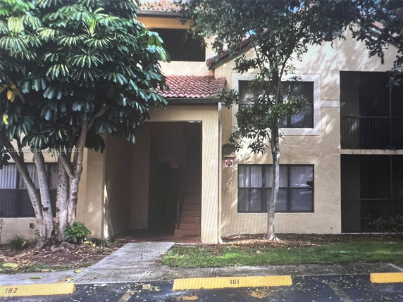 Front view of a two-story apartment building with stair access and surrounding trees.