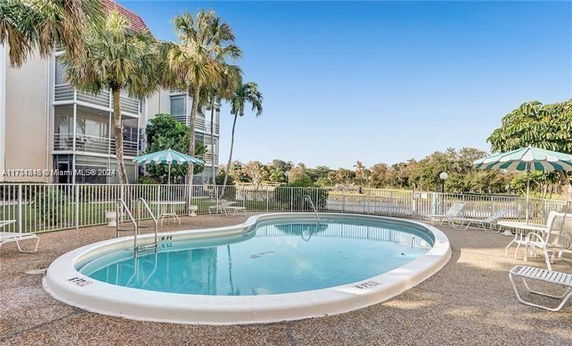 Outdoor swimming pool area with lounge chairs and umbrellas, adjacent to a multi-story building.