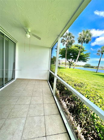 Outdoor view from a patio with tiled flooring, ceiling fan, and glass sliding doors, overlooking greenery and palm trees.