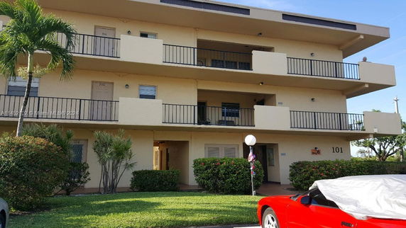 Front view of a three-story building with balconies and shrubbery.
