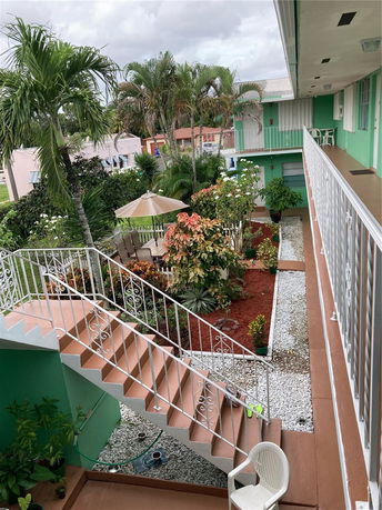 Outdoor view of a building complex with balconies and staircases, surrounded by lush vegetation.