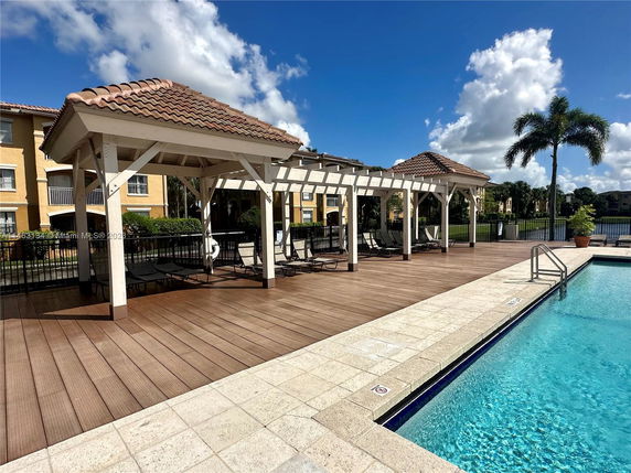 Outdoor area with a swimming pool, covered seating, and residential buildings in the background.