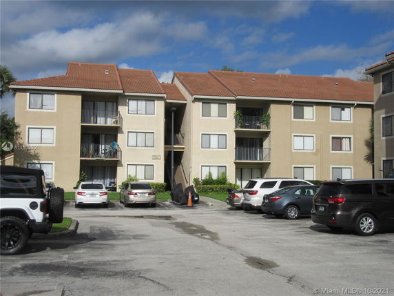 Front view of a multi-story apartment building with balconies and a parking area in front.