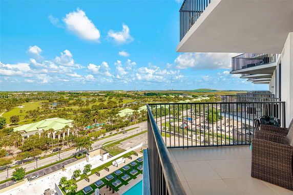 View from a high-rise balcony overlooking a landscape with green areas and buildings.