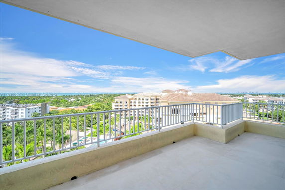 Panoramic view from a balcony overlooking buildings and greenery with a clear sky.