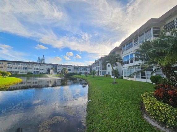 View of residential buildings with a pond and fountain in a landscaped setting.