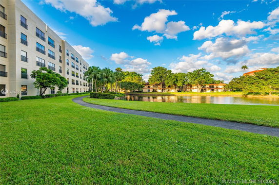 Landscape view with a pathway alongside a pond and a multi-story building on the left.