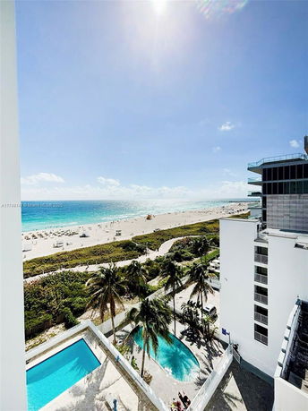 Wide-angle view of a beach and ocean seen from a high vantage point, with buildings and a pool in the foreground.