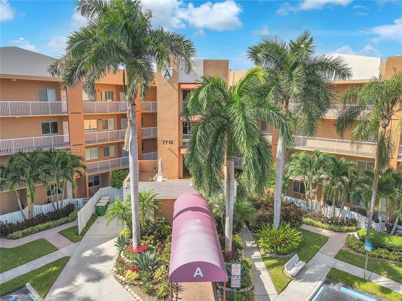 Front view of a multi-story building with balconies and surrounding palm trees.